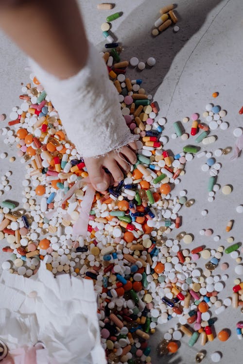 Free An overhead shot of a child's foot in a cast surrounded by scattered colorful pills indoors. Stock Photo